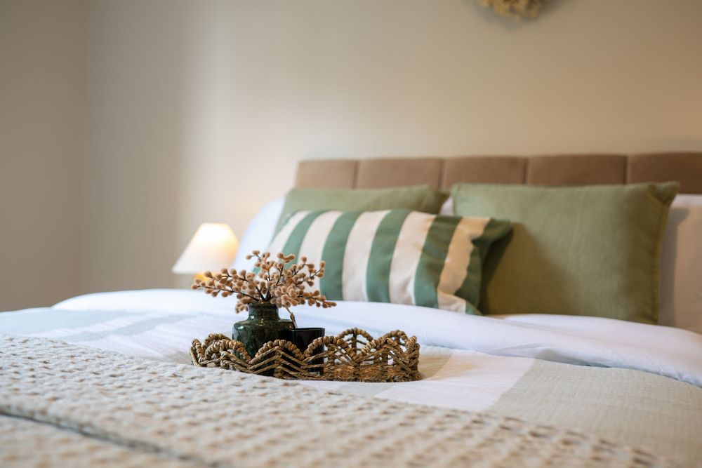 A decorative golden crown rests on a plush bed with green and white striped pillows in a sunlit bedroom.