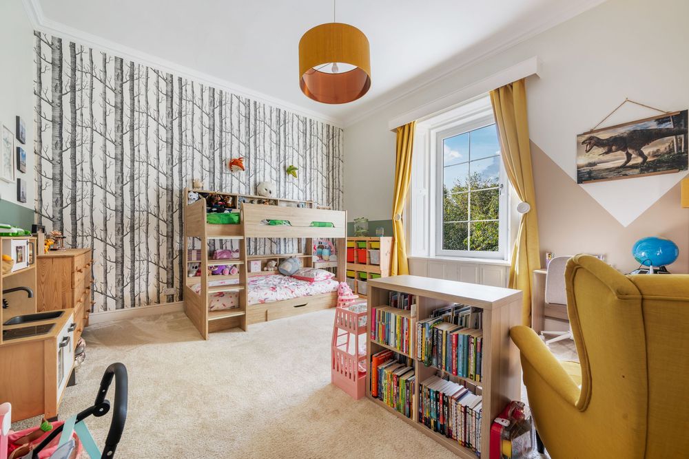 Children's playroom with birch tree wallpaper, bookshelves, and colorful toys arranged along the wall.