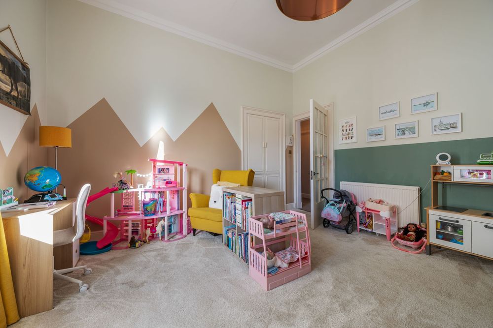 A children's playroom with pink dollhouses, toys and mountain-themed wall decor against neutral colored walls.