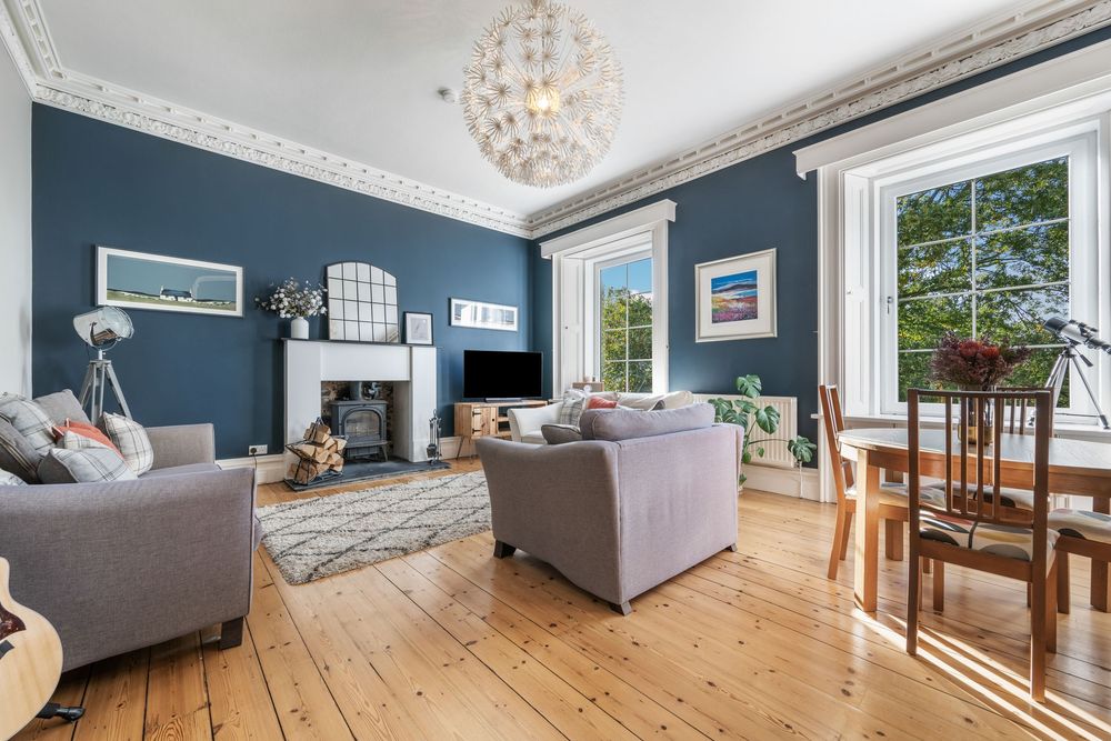 Elegant living room with deep blue walls, gray sofas, crystal chandelier, and natural wood flooring in a period property.