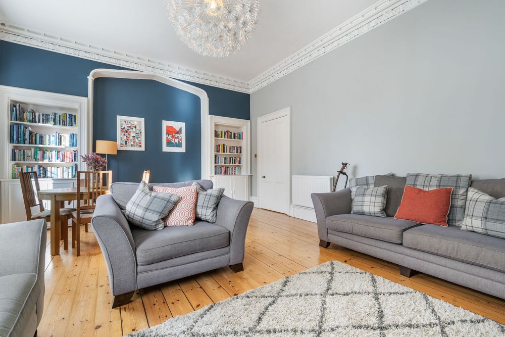 Contemporary living space featuring grey couches, patterned rug, and large windows with natural lighting.