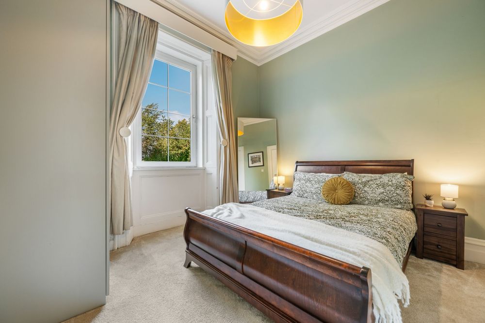 Spacious master bedroom with dark wood furniture, sage green walls, and natural light streaming through windows.