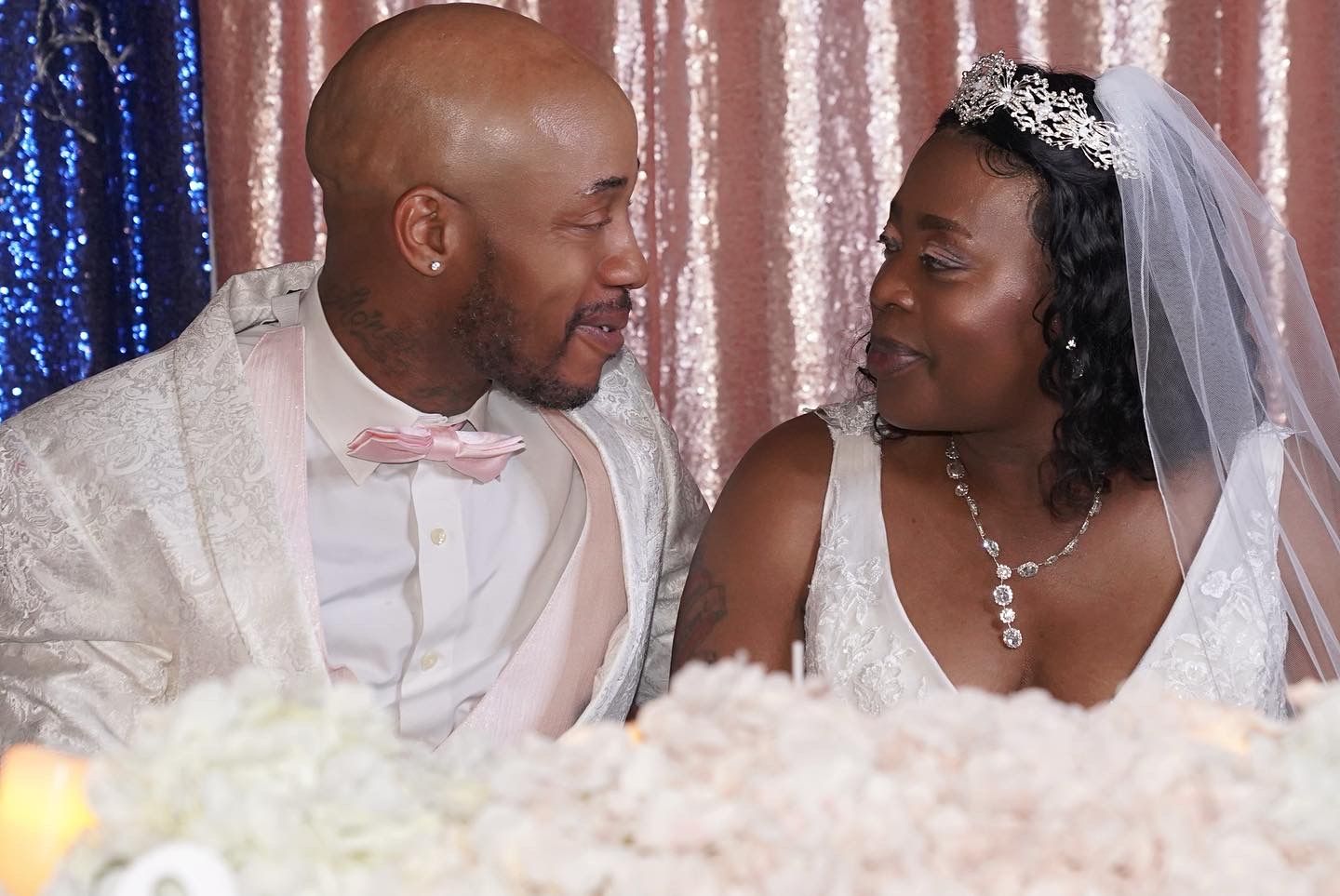 Newlyweds share a loving look at their wedding reception with sparkly backdrop and white decorations.