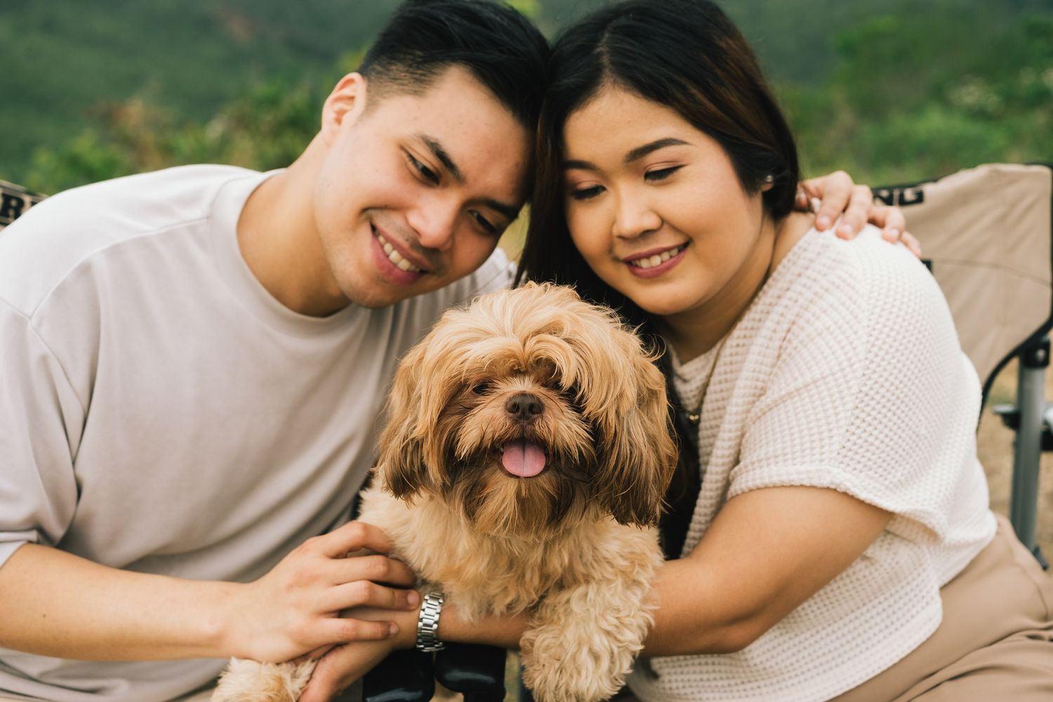 Happy couple cuddling with their smiling brown fluffy dog in casual outdoor setting.