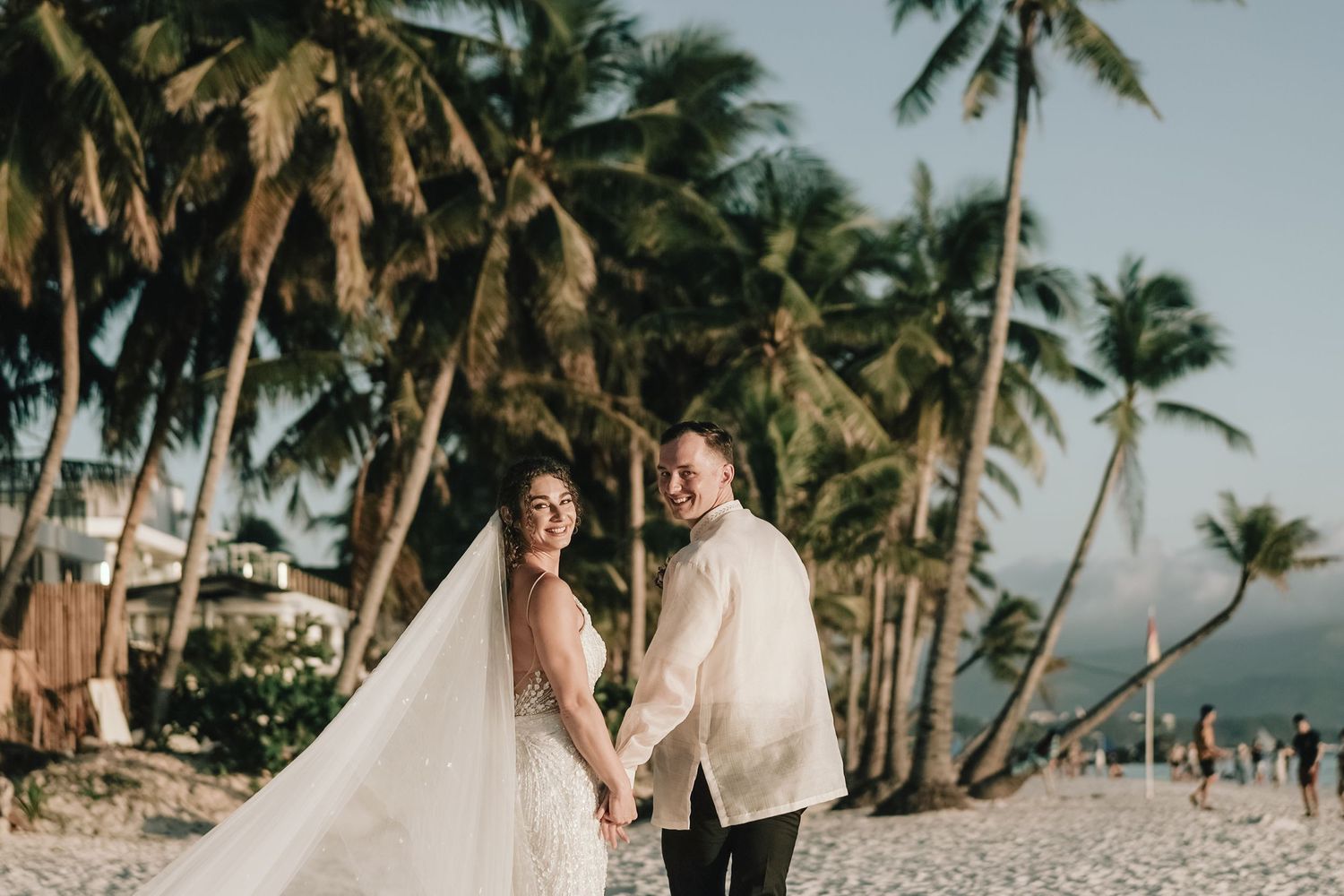 A newlywed couple poses on a tropical beach with palm trees and ocean views.