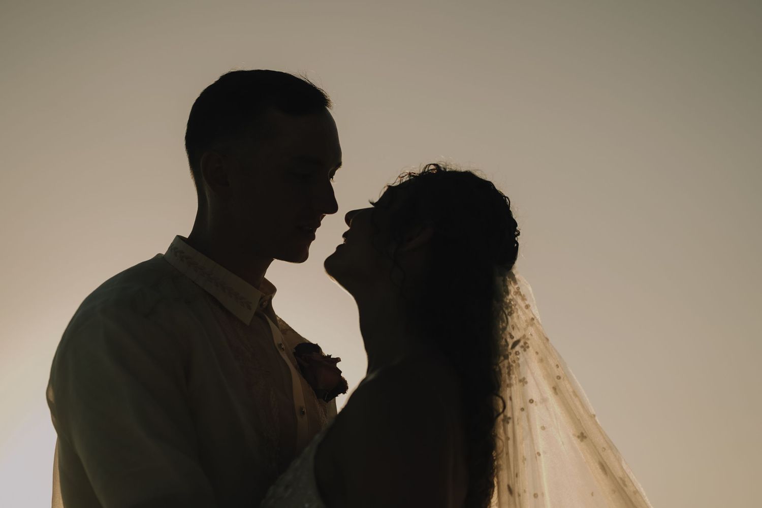 A romantic silhouette portrait of a couple embracing on their wedding day with a flowing veil.