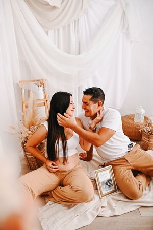 A couple shares a tender moment during a maternity photoshoot, sitting together with a sonogram photo nearby.