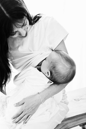 Black and white photo of a mother tenderly breastfeeding her newborn baby, wrapped in white cloth.