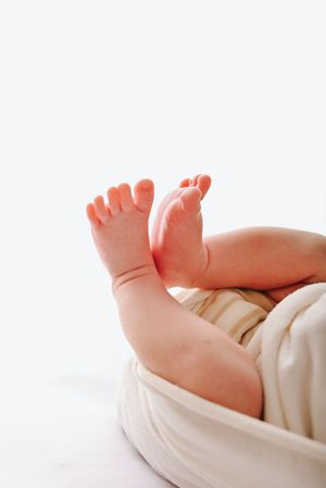 Close-up of tiny newborn baby feet raised up, wrapped in a soft white blanket.