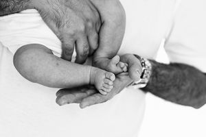 Black and white photo of a man cradling a newborn baby's tiny feet in his hands.