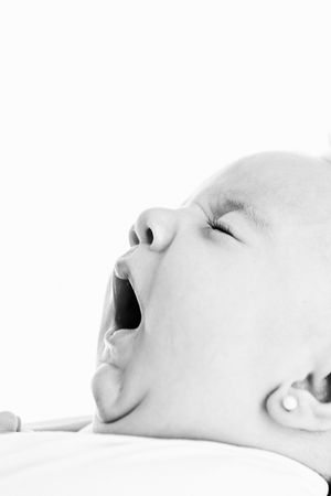 Black and white close-up photo of a yawning baby with eyes closed, lying on a white background.