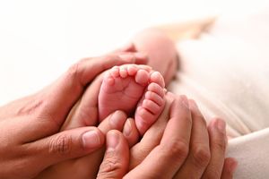 Adult hands gently cradling tiny newborn baby feet in a tender, loving close-up photo.
