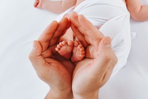 Close up of adult hands cradling tiny baby feet wrapped in white fabric.