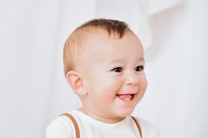 Happy baby in white clothing shows four different playful expressions while sitting against white background.