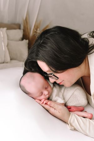 Tender moment between mother and sleeping newborn on white bedding.