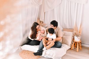 Family sharing intimate moment together on floor mattress with white drape backdrop.