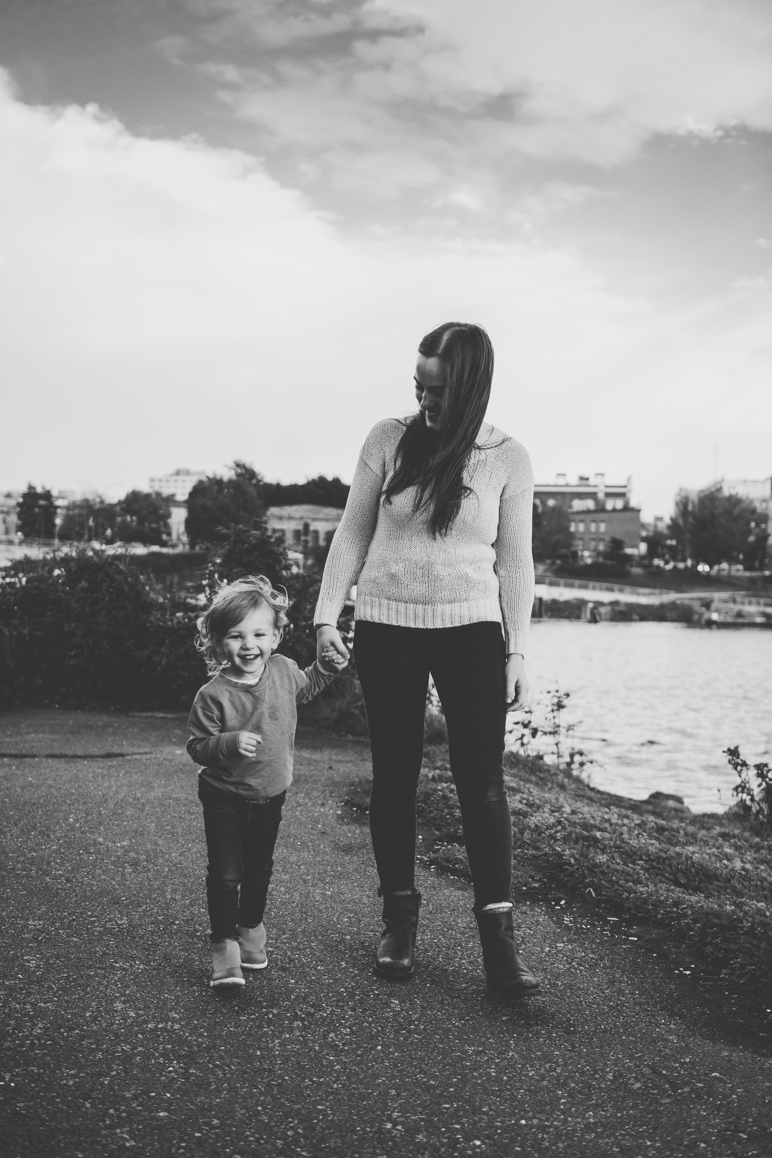 Adult and child walking hand in hand along a waterfront path.