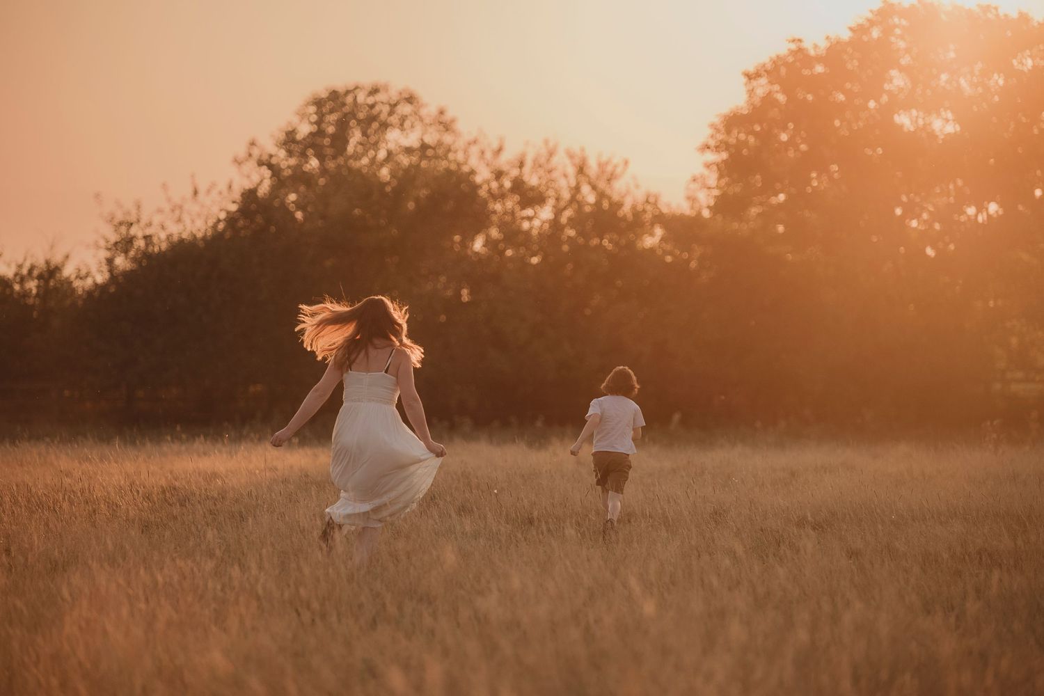 Two figures running joyfully through a golden wheat field at sunset with hair blowing in the wind.