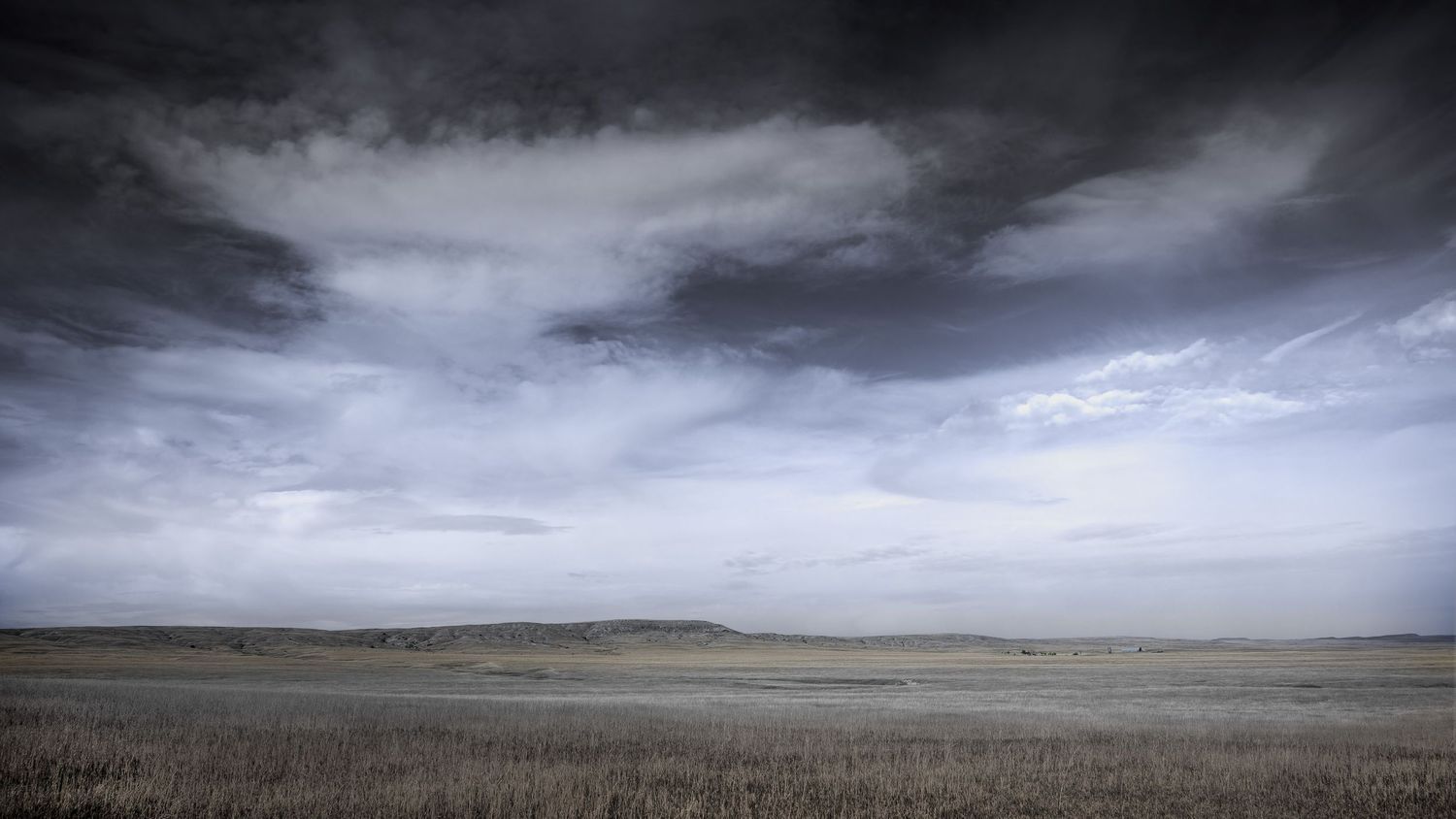 Dramatic storm clouds gather over rolling prairie grasslands.