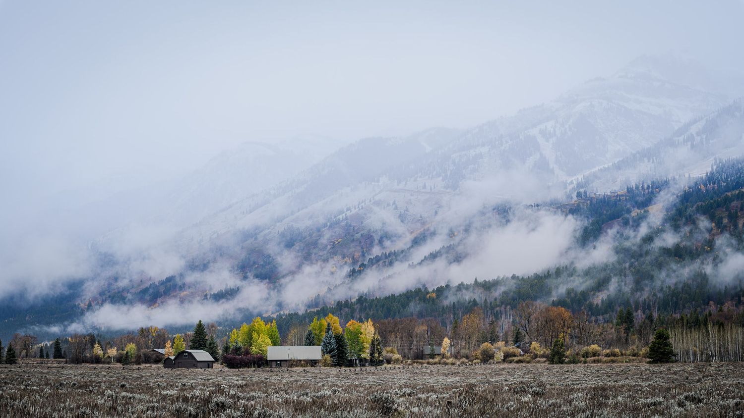 Misty mountains loom over a valley with autumn trees and scattered buildings in the foreground.