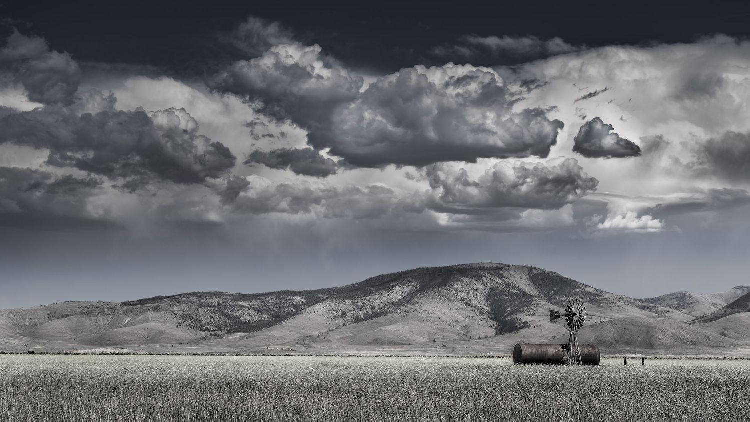 Dramatic clouds hover over rolling hills with a windmill silhouetted against the landscape.