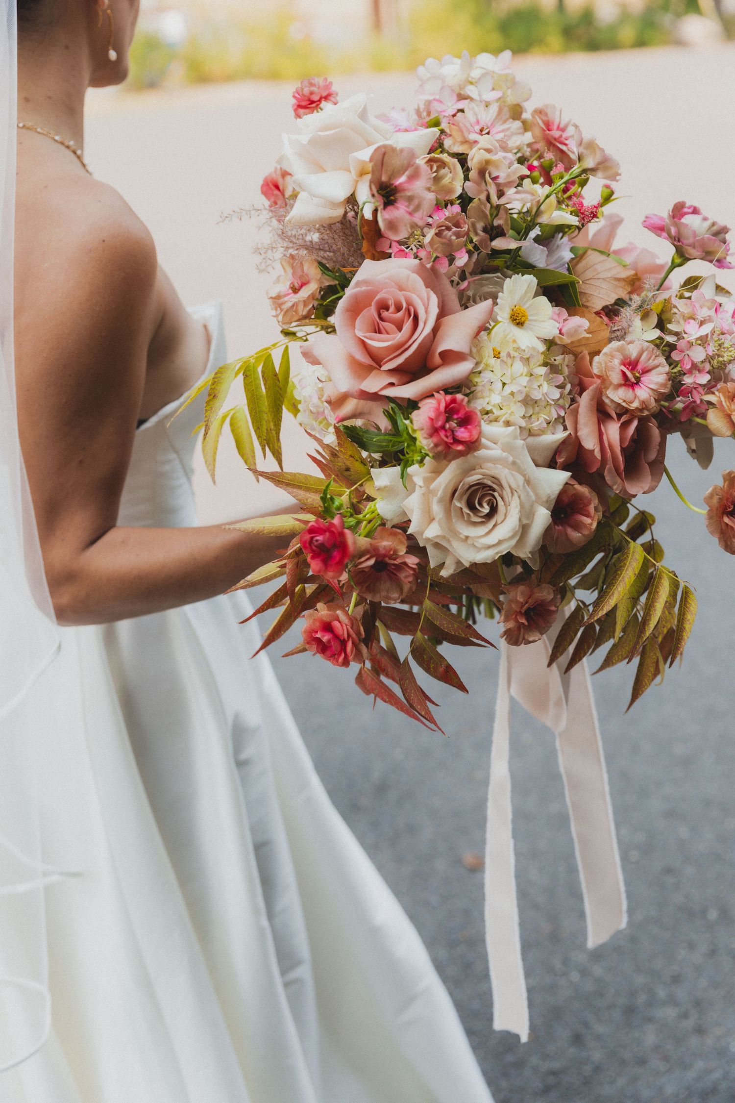 An elegant bridal bouquet featuring pink roses and mixed flowers with flowing ribbons.