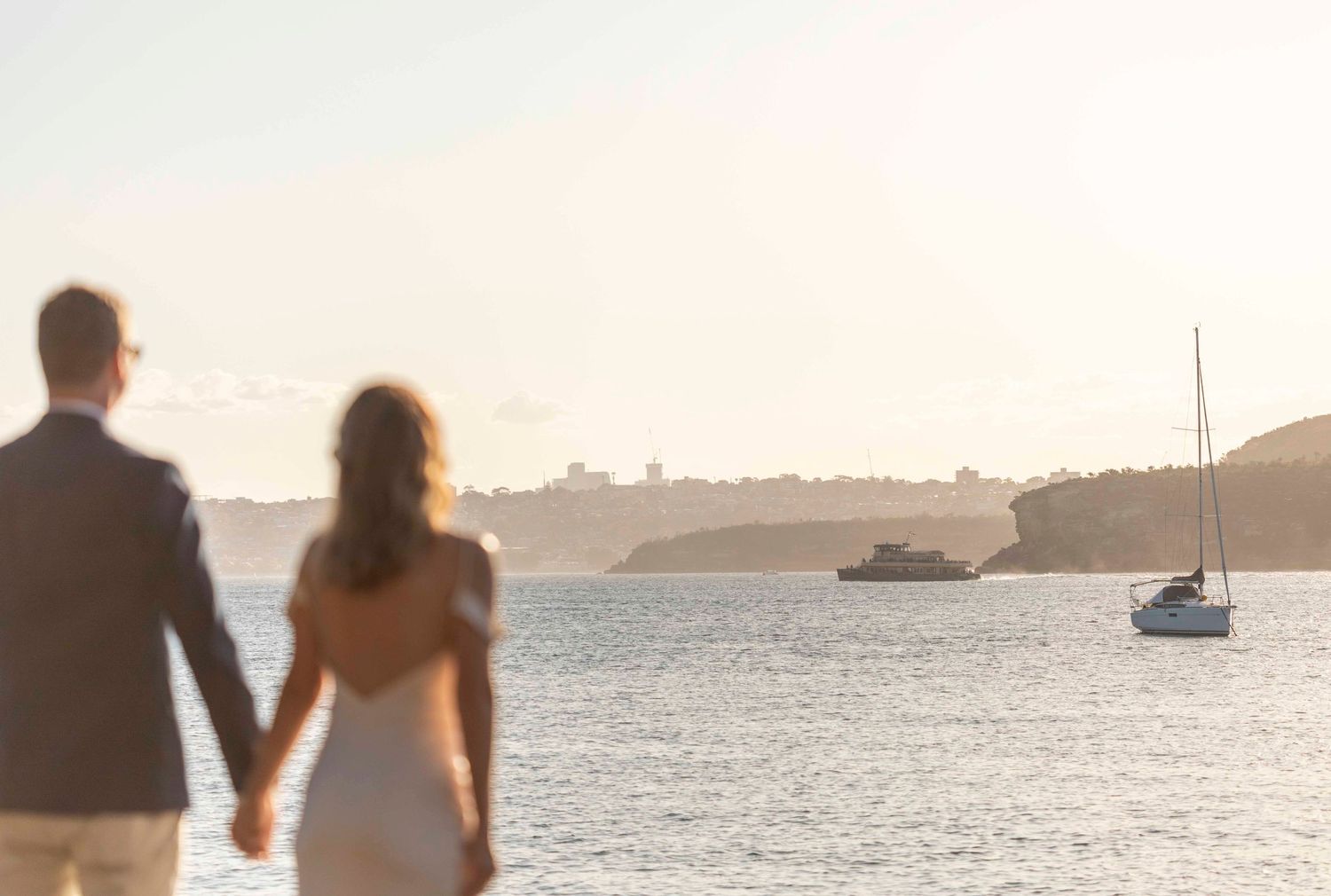Silhouetted couple watching sunset over harbor with boats in the distance.