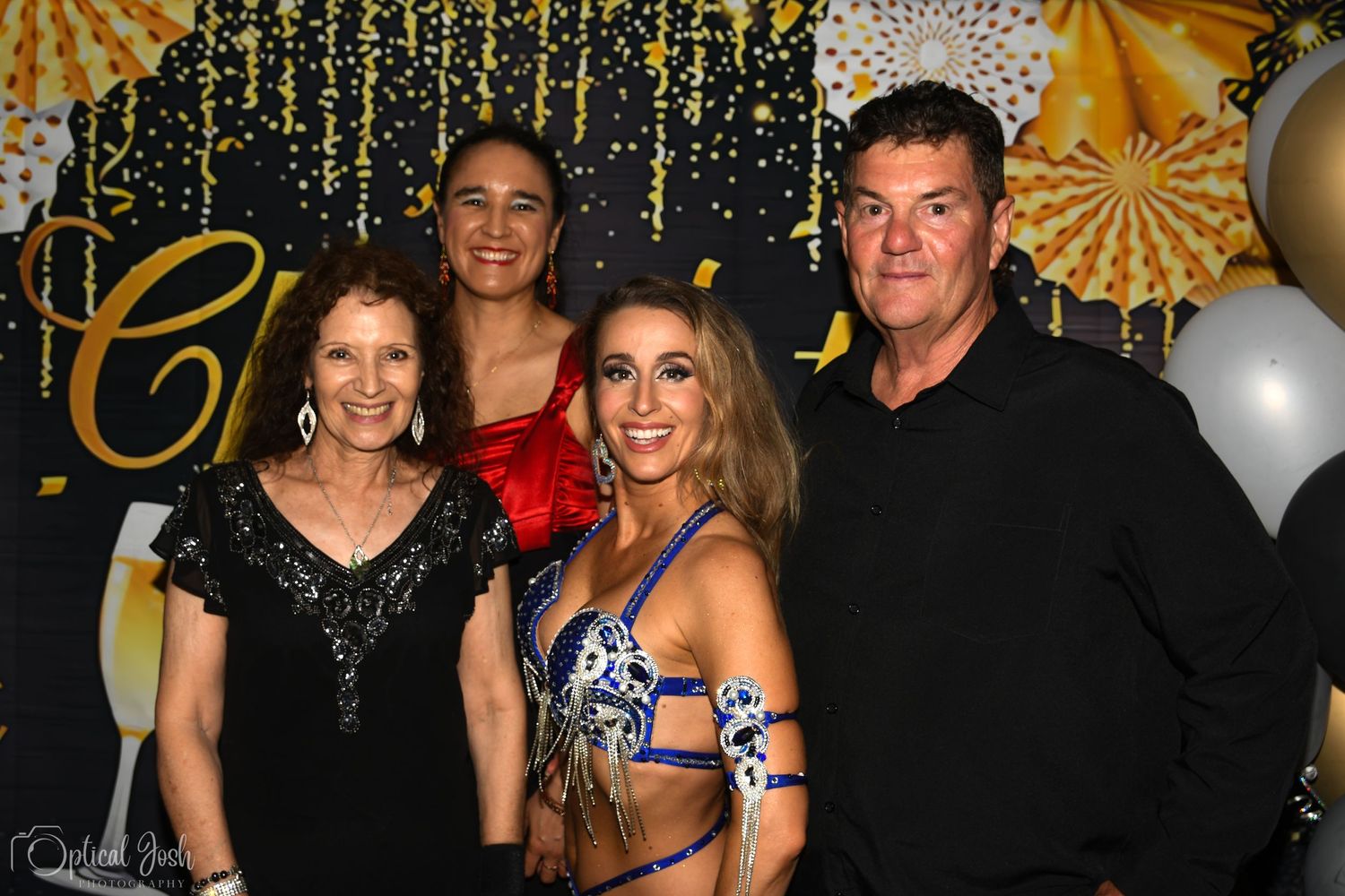 Group photo against a festive gold and black backdrop with balloons and decorative lighting.