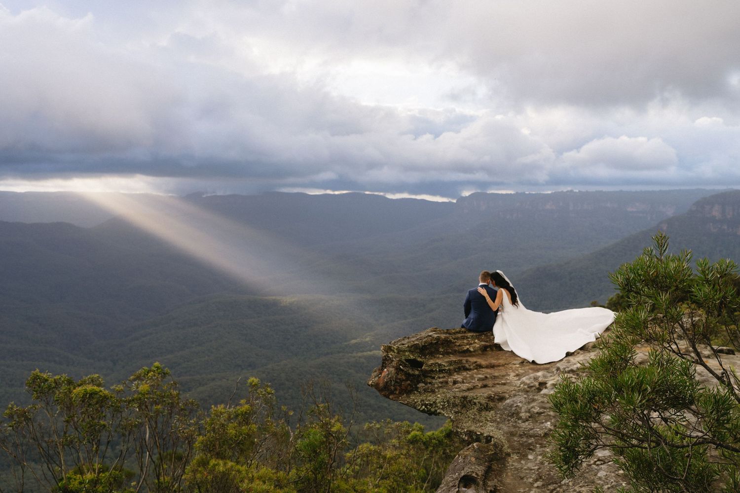 Scenic mountain vista with dramatic sunbeams breaking through clouds over valley landscape.