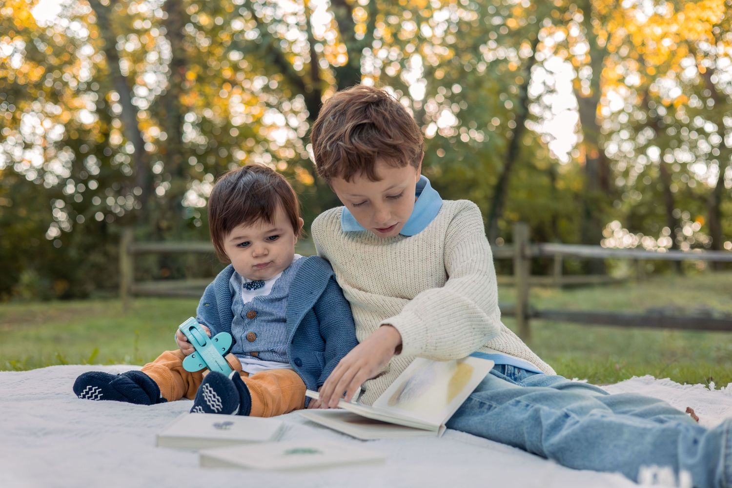 2 brothers read a book together on a blanket in the park.