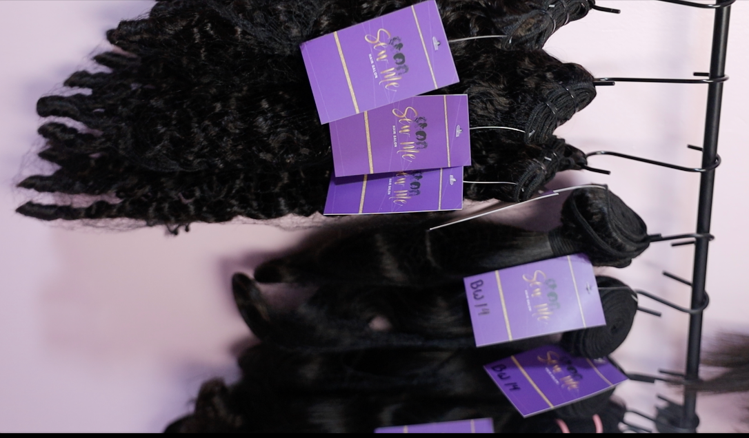 Black hair bundles displayed on a rack with purple brand labels attached, showcasing premium hair extensions.