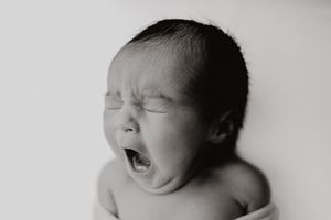 Black and white newborn photo of a yawning baby with eyes closed, captured in a serene studio setting. -- Sara Prue Photography Denver