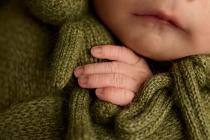 Close-up of a newborn baby's tiny hand resting on a soft green knitted wrap. -- Sara Prue Photography Denver