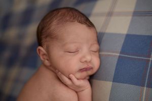 Peaceful newborn baby sleeping on a blue plaid blanket with tiny hands tucked under chin. -- Sara Prue Photography Denver