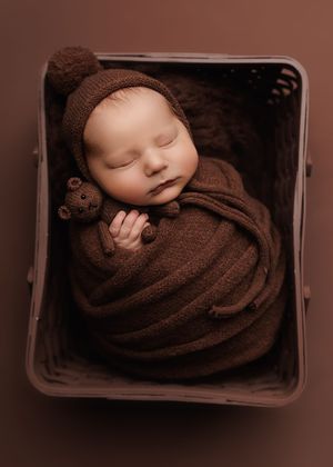 Sleeping newborn baby swaddled in a knit wrap with matching bonnet, holding a teddy bear in a wicker basket. -- Sara Prue Photography Denver