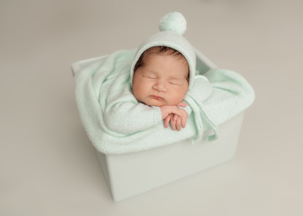 Sleeping newborn baby in mint green knit outfit and hat resting in a white box with soft blanket. -- Sara Prue Photography Denver