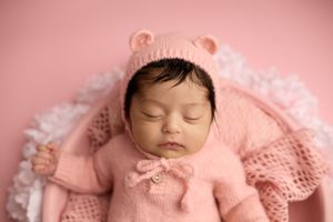 Newborn baby sleeping peacefully in pink knit bear bonnet and matching outfit on soft pink background. -- Sara Prue Photography Denver