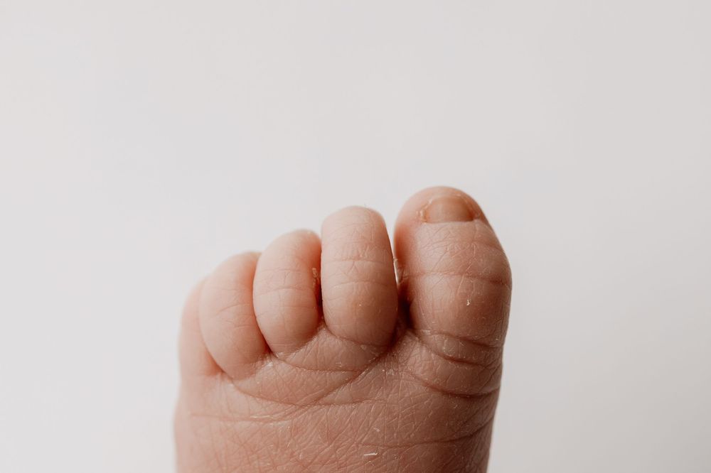 Close-up of a baby's small clenched fist with tiny fingers and peeling skin on a white background.  -- Sara Prue Photography Denver