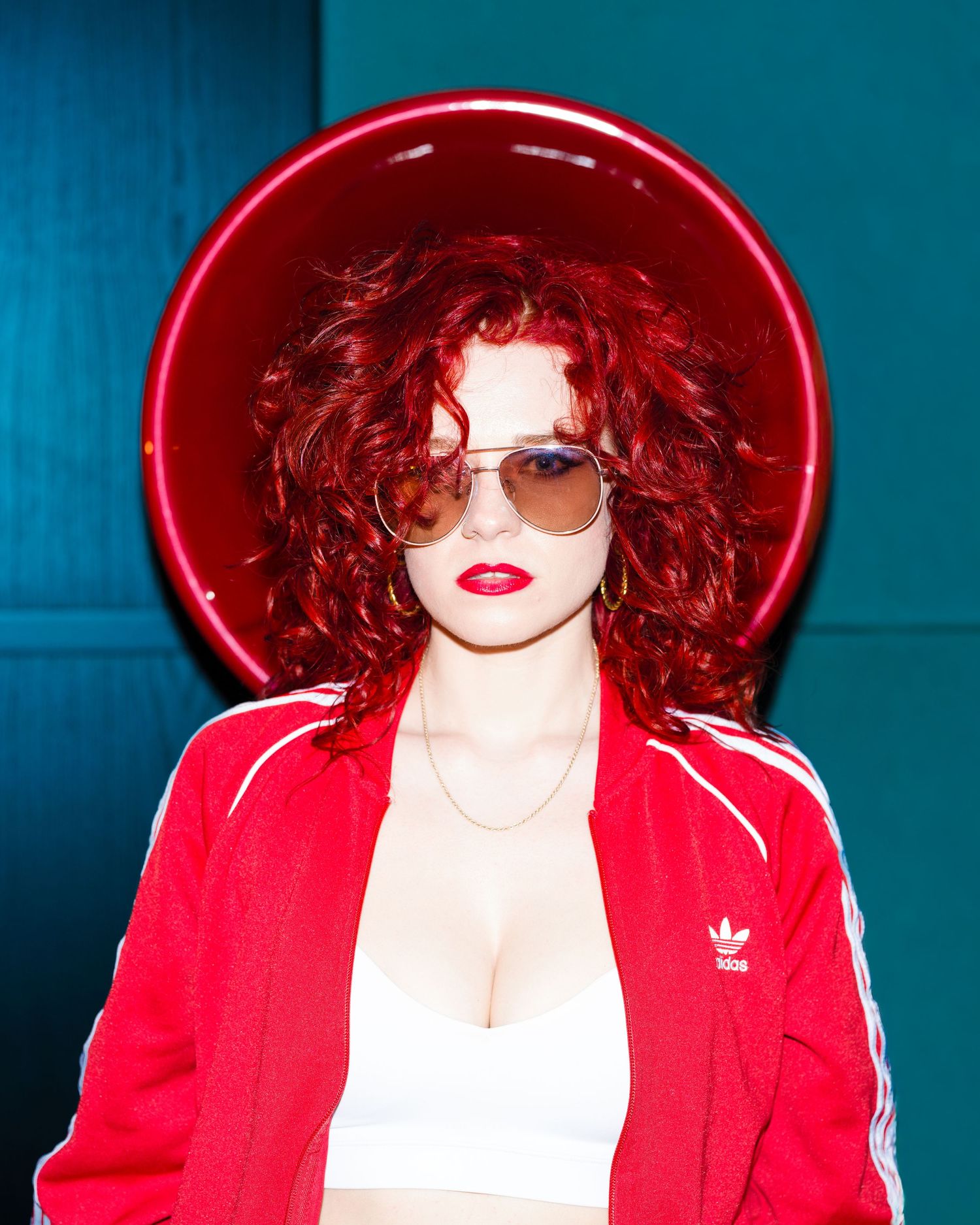 Model in a wide-brimmed red hat and red jacket posing against a teal backdrop, editorial fashion photography