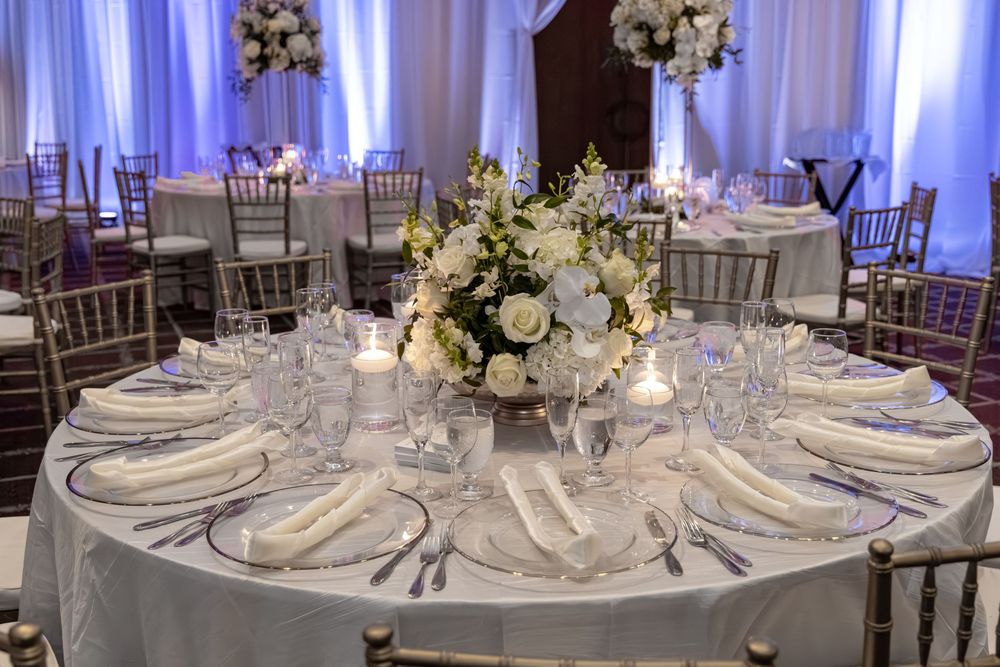 Elegant wedding reception table with white floral centerpiece, fine china, crystal glasses, and candles in a softly lit ballroom.