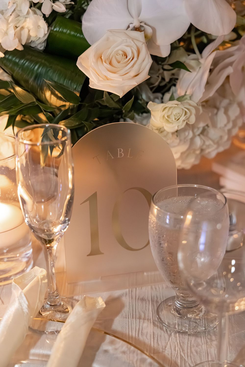 Elegant wedding table setting with white roses, orchids, champagne flutes, and a gold Table 10 sign.