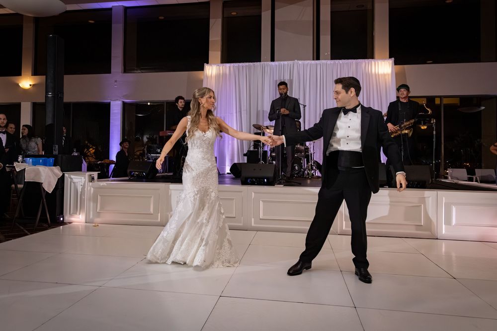 Bride and groom share their first dance on a white dance floor with a live band performing behind them at their wedding reception.