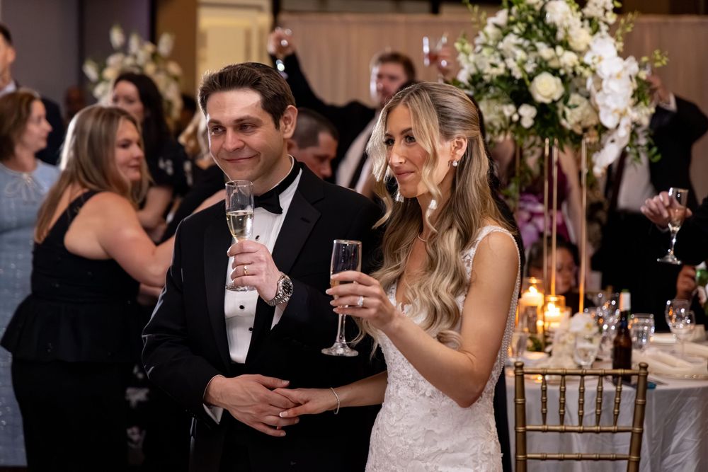 Bride and groom smiling and holding champagne glasses at elegant wedding reception with floral arrangements.
