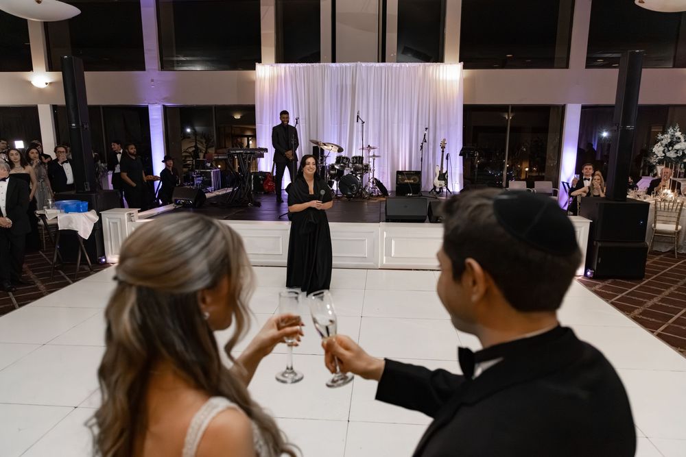 Bride and groom toasting champagne on white dance floor at elegant wedding reception with live band.