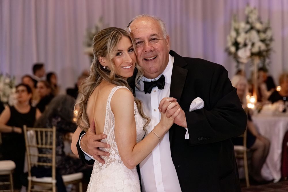 Bride and older gentleman share a joyful father-daughter dance at elegant wedding reception.