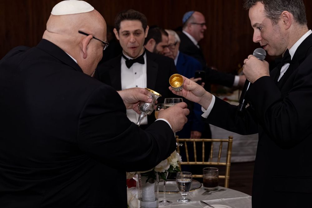 Men in tuxedos toasting with glasses at a formal black-tie event dinner reception.