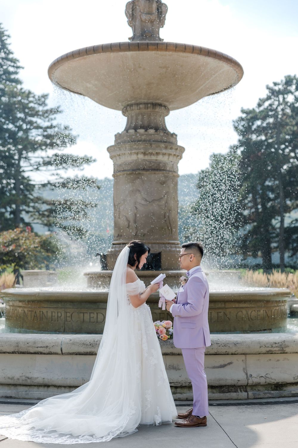 Bride and groom standing in front of the fountain at gage park reading their private vows during their wedding photos in hamilton, ontario.