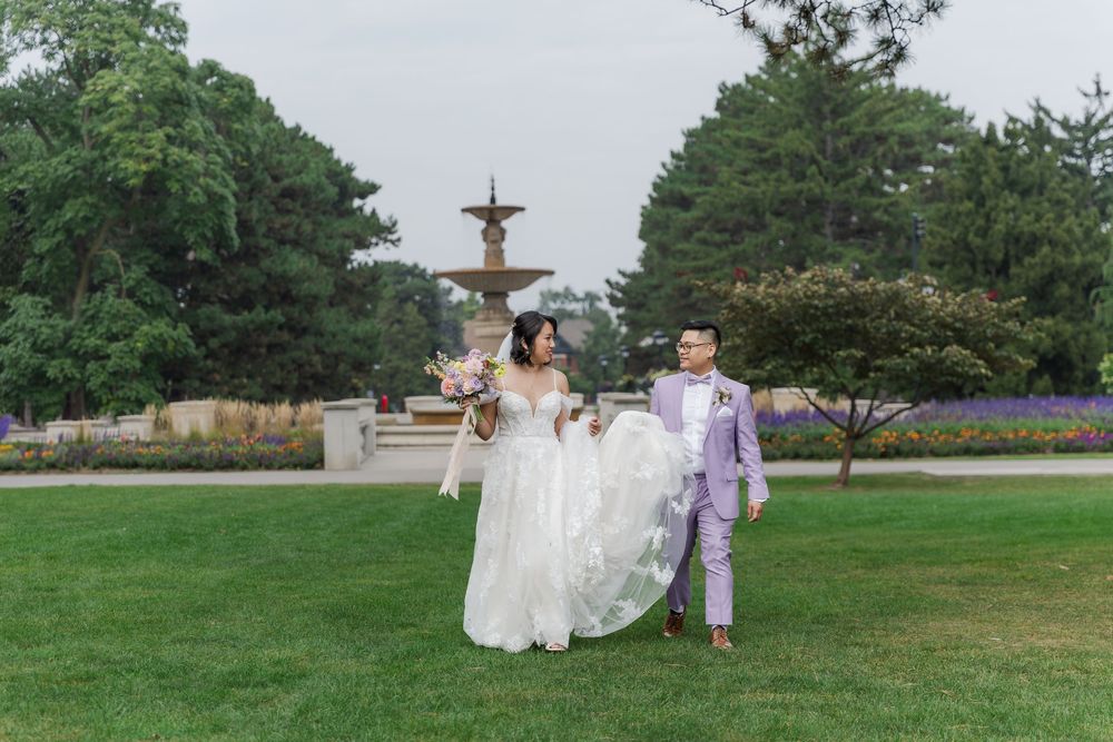 Bride and groom walking through the grass in gage park during their hamilton, ontario wedding photos.