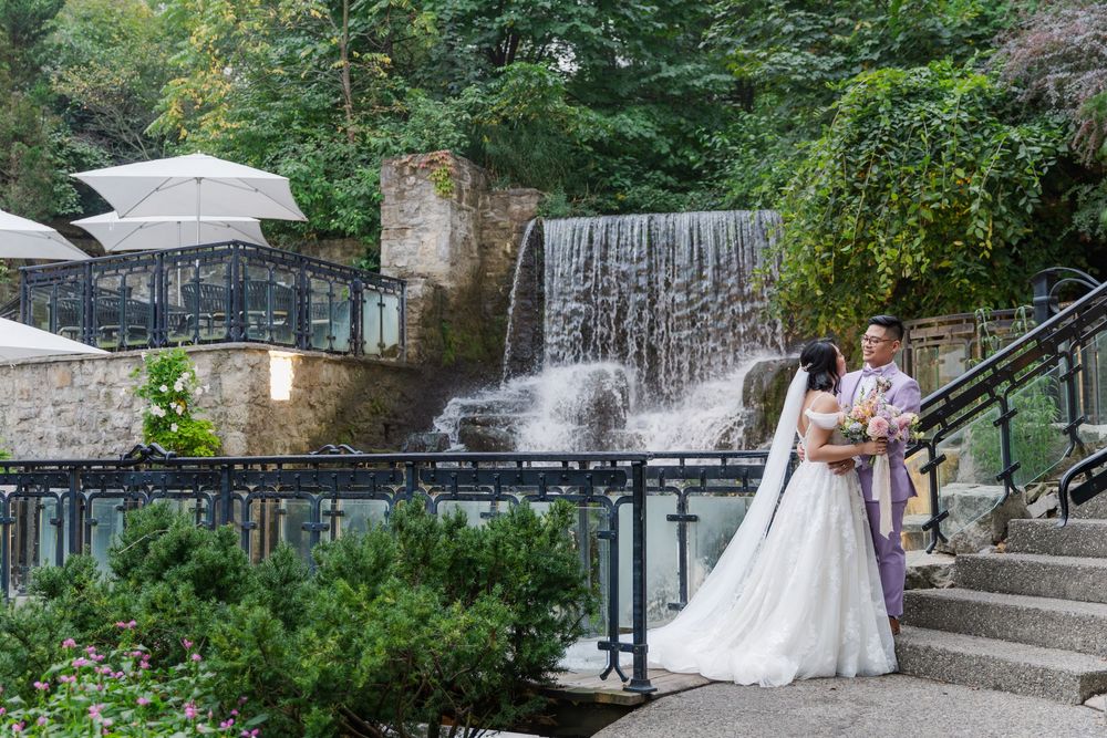 Candid wedding photo of bride and groom looking at each other beside the waterfall at the ancaster mill in hamilton, ontario.