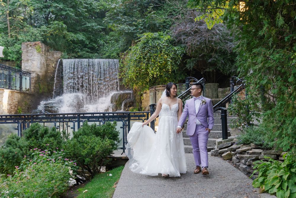 Relaxed wedding photo of bride and groom walking alongside the waterfall at the ancaster mill in hamilton, ontario.